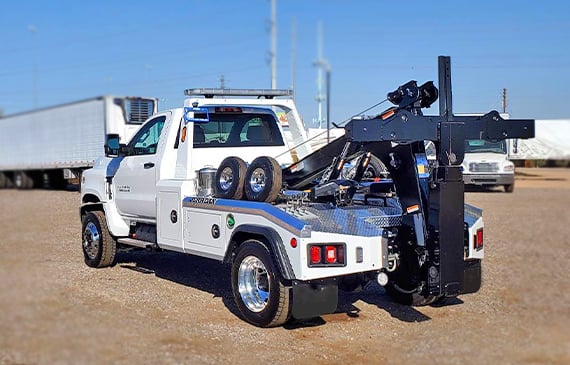 A brand new white light-duty integrated tow truck is parked on a dirt lot during a sunny day.